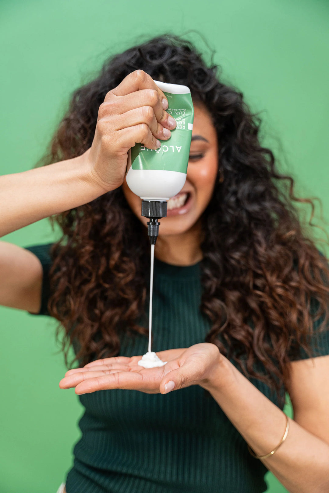 Femme aux cheveux bouclés versant le revitalisant boucles Alcôve dans sa main, illustrant la texture crémeuse du produit.
