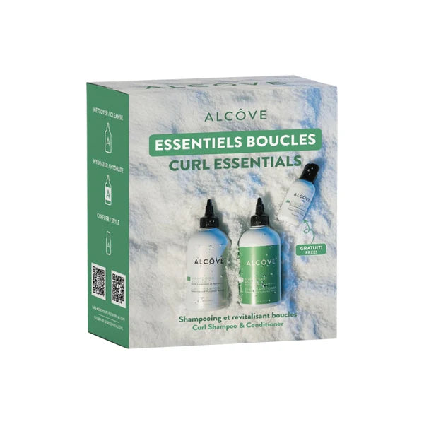 Coffret cadeau Alcôve « Essentiels Boucles » contenant un shampoing, un revitalisant et un activateur de boucles en format découverte, posé sur un fond texturé blanc doux.