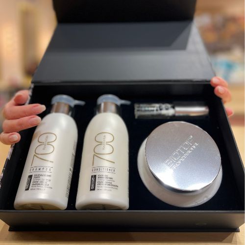 Coffret ouvert Biotop 700 contenant un shampoing 330ml, un revitalisant 330ml, un masque 350ml et un sérum 30ml. Produits capillaires professionnels à la kératine pour cheveux épais, secs ou abîmés, présentés dans un écrin noir élégant avec mains visibles tenant le couvercle.