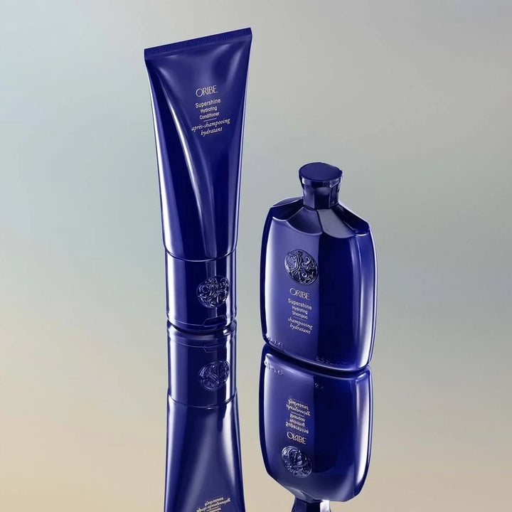 Duo shampoing et après-shampoing ORIBE Supershine, flacons bleu nuit à effet miroir, avec reflet sur surface brillante, ambiance élégante et sophistiquée.