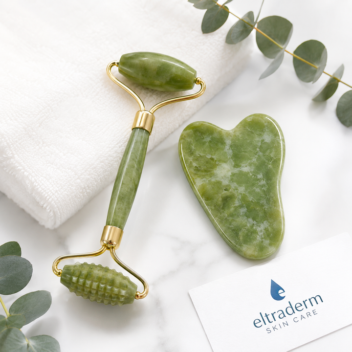 Rouleau de jade Xiuyan Eltraderm à double embout et Gua Sha facial en jade vert marbré présentés sur fond marbre blanc avec serviette et feuillage décoratif. Outils de massage du visage conçus pour stimuler la circulation, favoriser le drainage lymphatique et améliorer l'apparence de la peau.