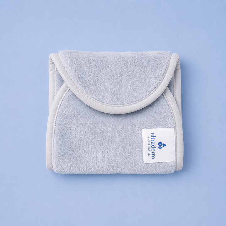 Serviette nettoyante pour le visage Eltraderm en microfibres de polyester gris pâle, pliée avec rabat arrondi et étiquette de marque visible, présentée sur fond bleu clair dans un visuel produit professionnel.