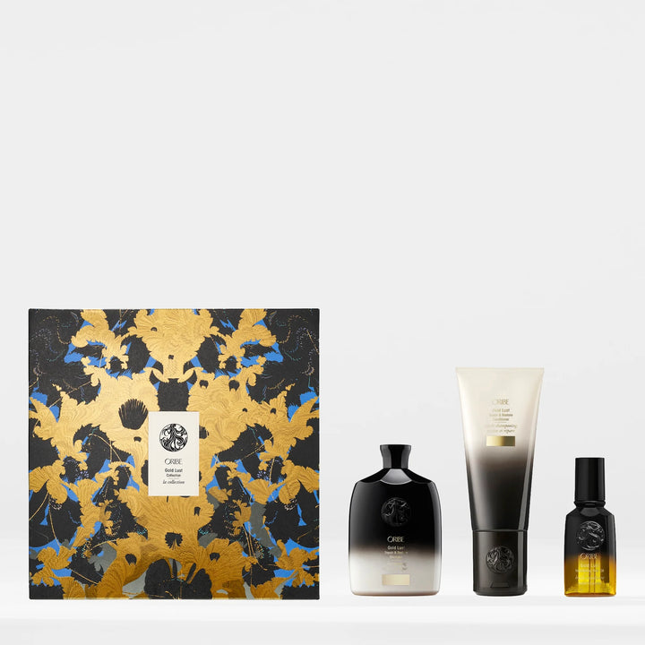 Coffret Oribe Gold Lust sur fond blanc, avec les trois soins cheveux posés à côté : shampooing noir et blanc, revitalisant noir et crème, et huile capillaire dans un flacon ambré. Boîte ornée de motifs dorés et bleus.