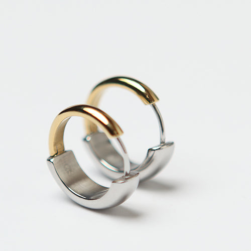 Paire de boucles d’oreilles créoles en acier inoxydable bicolore, avec moitié en argent poli et moitié en finition or jaune. Design épuré et contemporain, posées debout sur fond blanc.
