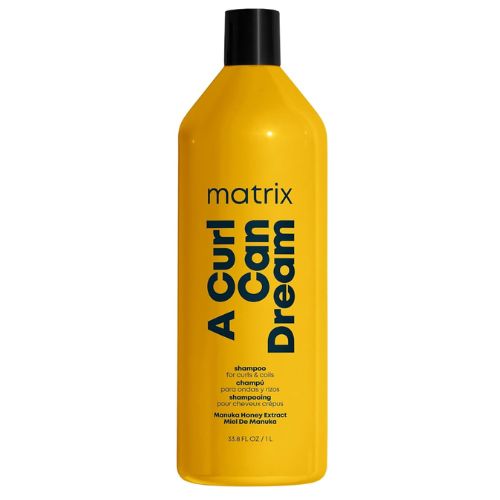 Bouteille jaune 1L du shampoing Matrix A Curl Can Dream, conçu pour les cheveux frisés et crépus. Enrichi en miel de Manuka, ce shampoing nettoie sans agresser les boucles.