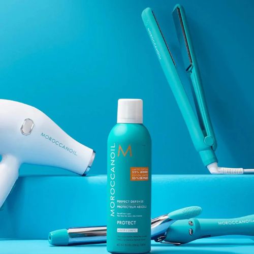 Flacon du Protecteur Absolu Moroccanoil 300 ml posé devant un sèche-cheveux, un fer à lisser et un boucleur turquoise sur fond bleu. Spray thermo-protecteur cheveux, flacon turquoise avec bouchon blanc et étiquette orange, idéal pour protéger la fibre capillaire avant l’utilisation d’outils chauffants jusqu’à 230 °C. Soin enrichi en huile d’argan, finition professionnelle.