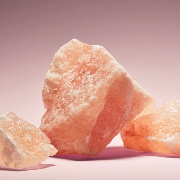 Cristaux de sel rose de l’Himalaya bruts posés sur un fond rose doux, texture minérale naturelle utilisée en cosmétique et parfumerie pour ses propriétés purifiantes.