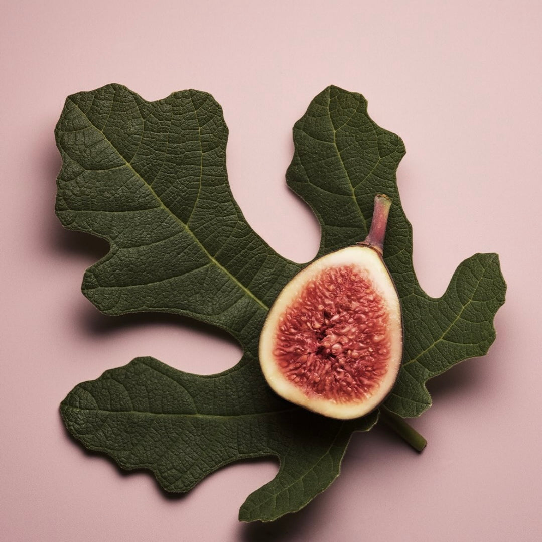 Figue fraîche coupée en deux posée sur une grande feuille verte, montrant sa chair rouge et ses graines, ingrédient naturel souvent utilisé dans les parfums et soins sensoriels.