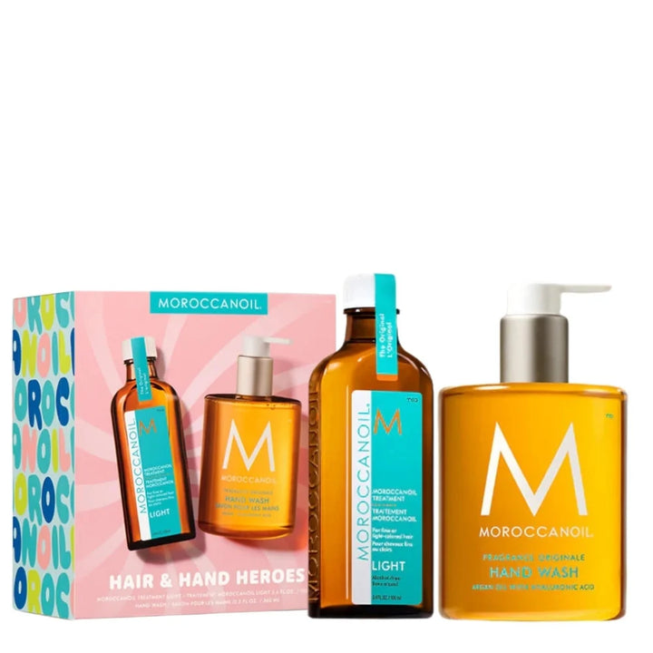 Coffret Moroccanoil Hair & Hand Heroes Light en édition limitée comprenant le Traitement Moroccanoil Light pour cheveux fins ou clairs et le savon pour les mains Fragrance Originale dans des bouteilles ambrées élégantes, présenté devant une boîte rose et turquoise au design coloré sur fond gris clair.