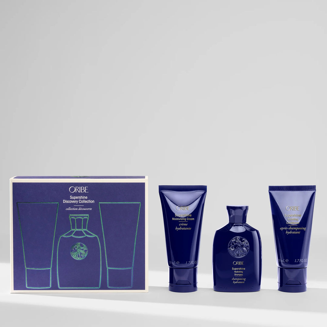 Coffret Oribe Supershine Discovery Collection avec shampooing hydratant, revitalisant et crème sans rinçage formats voyage disposés à côté de la boîte du coffret bleu signature.
