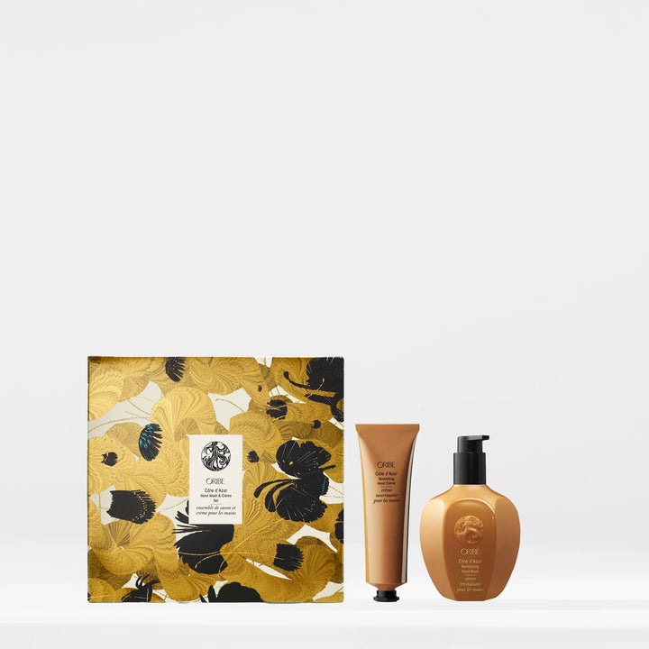Savon pour les mains et crème Oribe Côte d’Azur côte à côte devant un coffret fleuri doré et noir, sur fond blanc minimaliste.