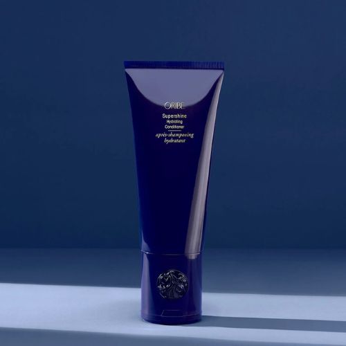 Tube de 200 ml de l'après-shampoing hydratant ORIBE Supershine, couleur bleu nuit brillante, logo en relief à la base, posé sur fond bleu studio, style minimaliste luxueux.