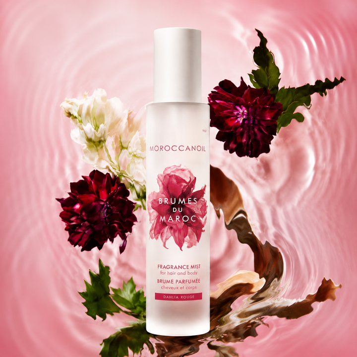 Flacon grand format Moroccanoil Brumes du Maroc Dahlia Rouge sur fond rose aquatique avec fleurs rouges et blanches élégantes et effet d’eau artistique.