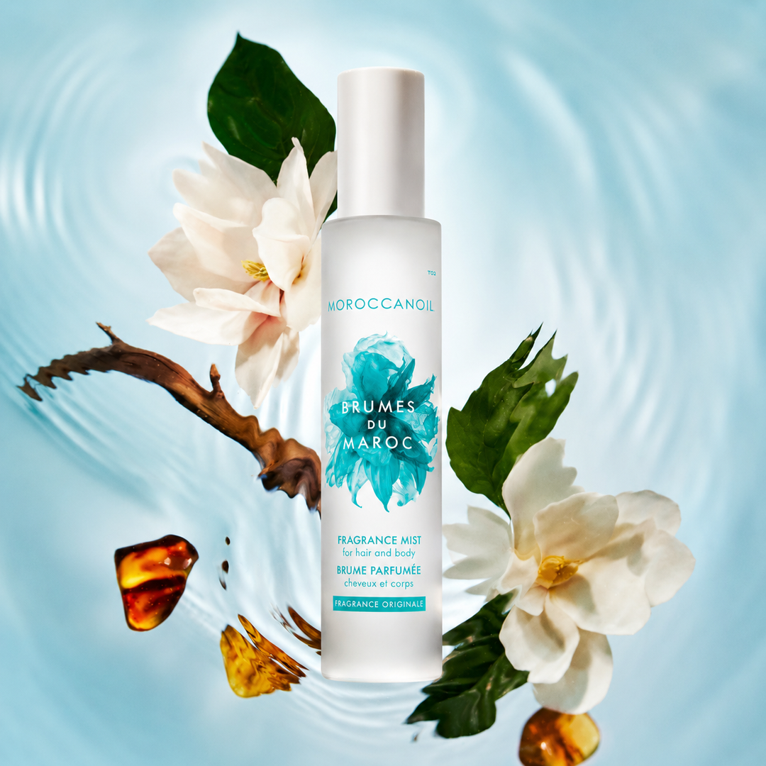 Flacon grand format Moroccanoil Brumes du Maroc Fragrance Originale avec fleurs blanches, feuilles vertes et accents ambrés sur fond bleu clair effet ondulation d’eau.