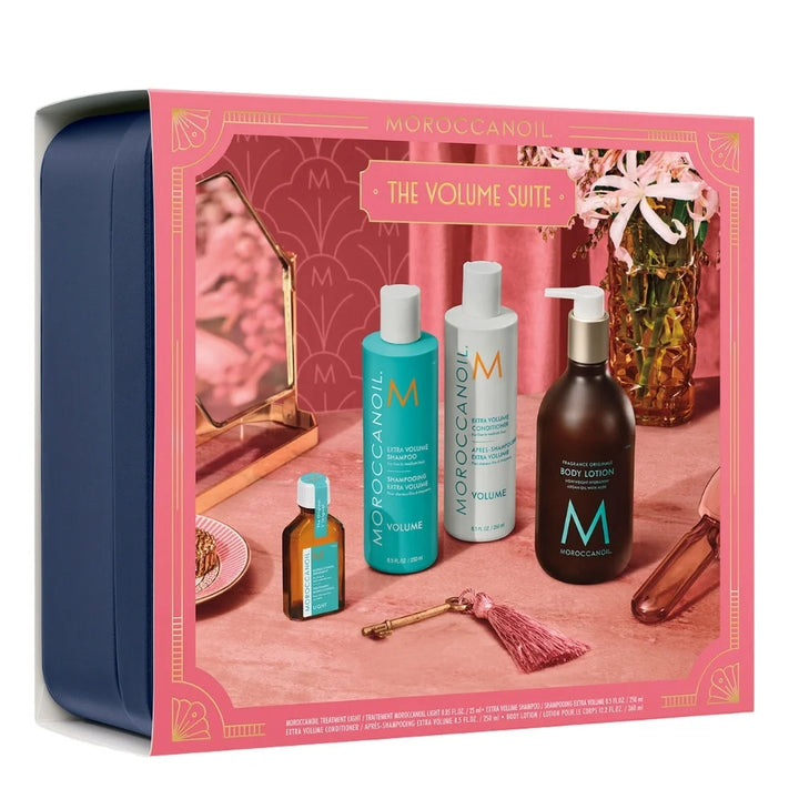 Ensemble Volume Moroccanoil avec shampooing et après-shampooing Extra Volume, Traitement Léger, lotion corps et coffret bleu marine sur décor rose.