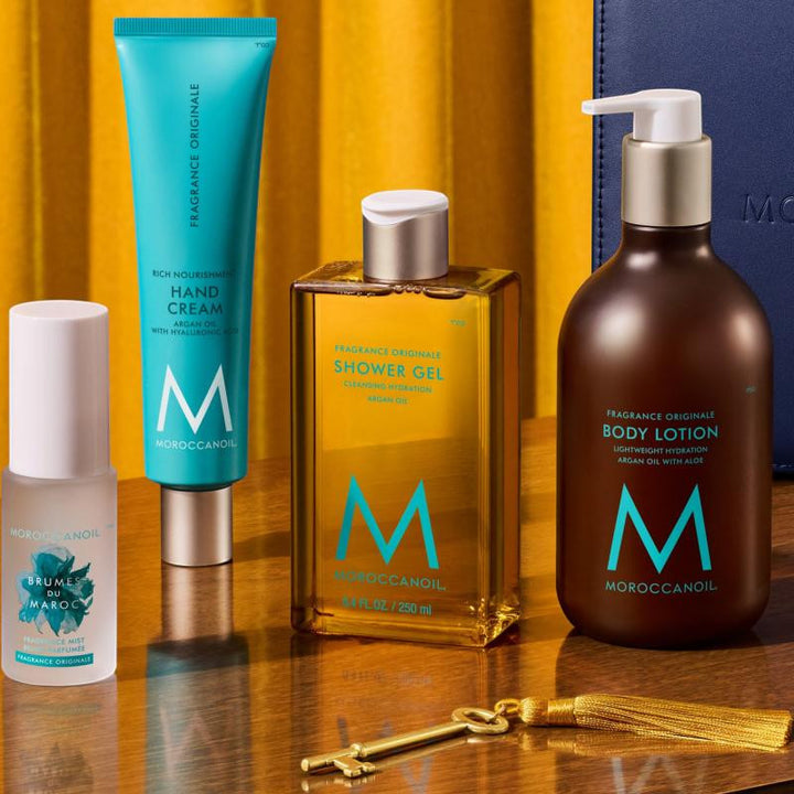 Soins corporels Moroccanoil Fragrance Originale comprenant Brumes du Maroc, crème mains, gel douche et lotion pour le corps sur décor doré.