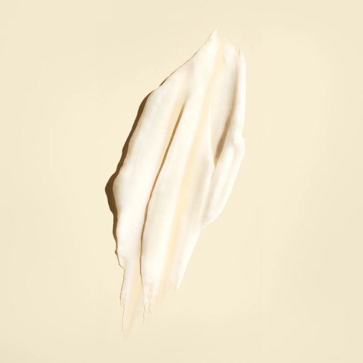 Texture crémeuse blanc ivoire de l'après-shampoing ORIBE Gold Lust Repair & Restore, étalée en une longue trace sur un fond beige clair.