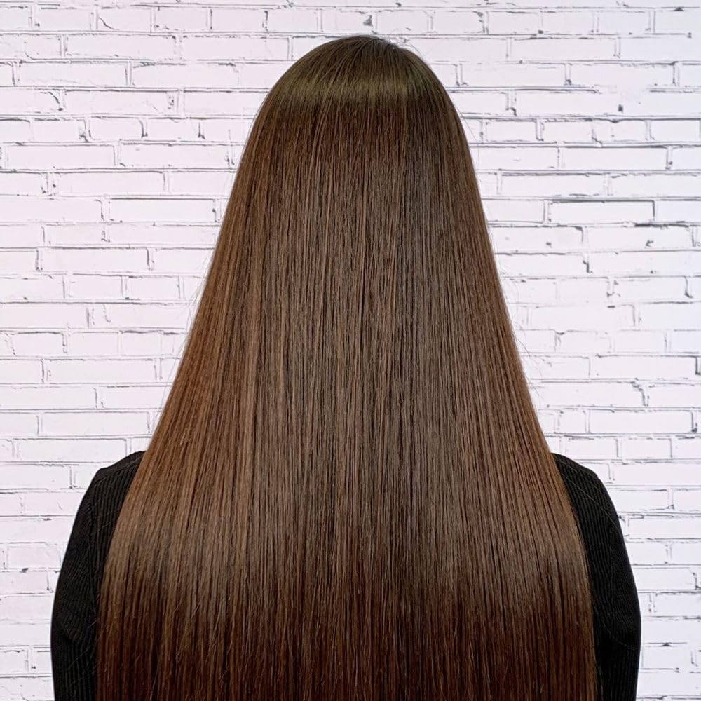 Vue arrière d’une chevelure longue, lisse et brillante de couleur châtain foncé, parfaitement coiffée, devant un mur de briques blanches. Les cheveux apparaissent doux, disciplinés et sans frisottis, résultat d’un lissage thermique.