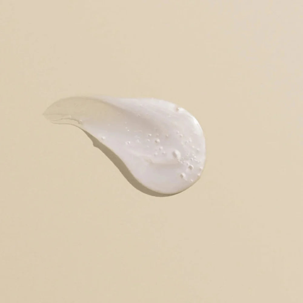 Texture crémeuse blanche nacrée du shampooing réparateur Rich Repair de Goldwell, illustrant sa formule riche et hydratante sur fond beige uni.