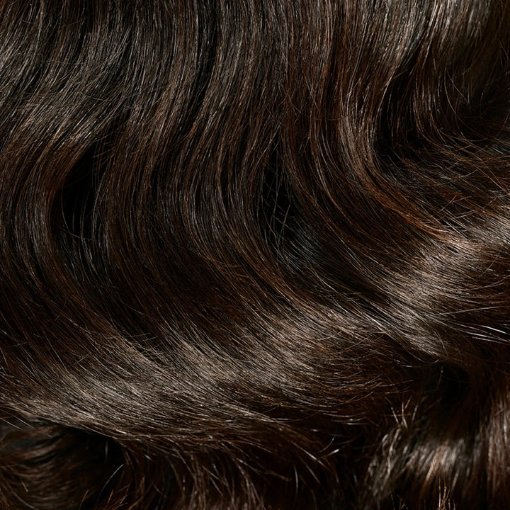 Gros plan sur des cheveux bruns foncés, ondulés et brillants, illustrant la douceur et l'éclat recherchés avec l'huile capillaire ORIBE Gold Lust.
