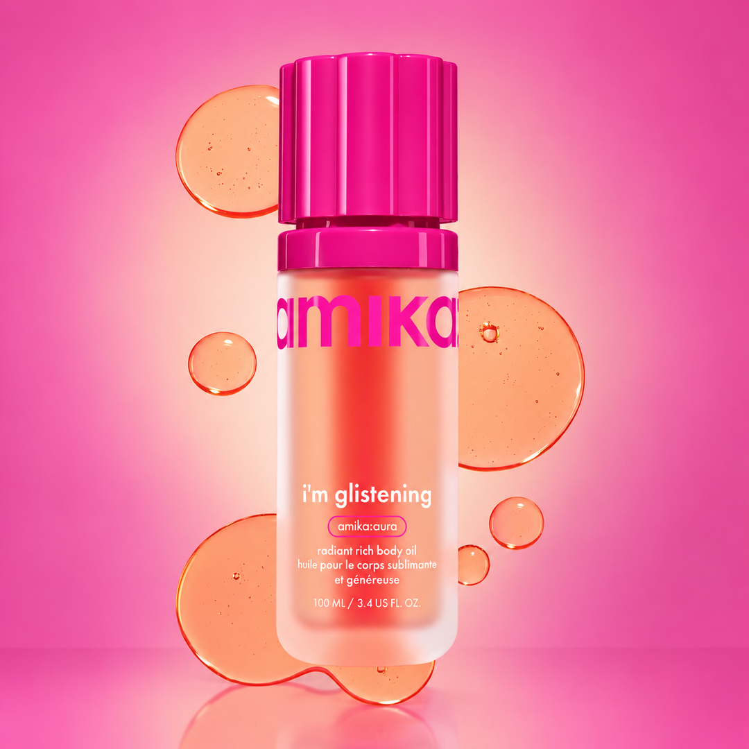 Huile pour le corps AMIKA I'm Glistening 100 ml en flacon rose, avec gouttes d'huile orangée sur fond rose et caractéristiques de la formule.