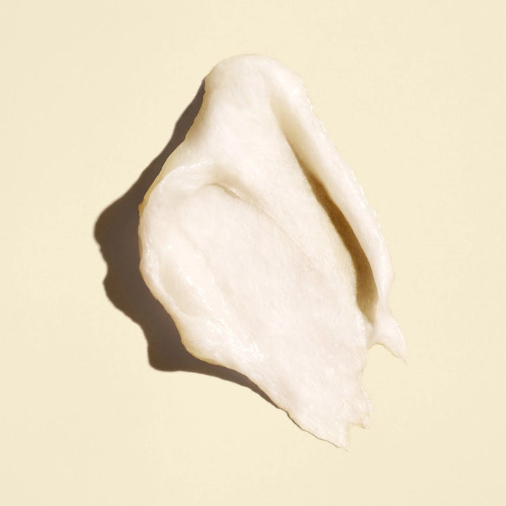 Texture riche et crémeuse blanc ivoire du masque capillaire ORIBE Gold Lust Transformative Masque, étalée en couche épaisse sur un fond beige clair.