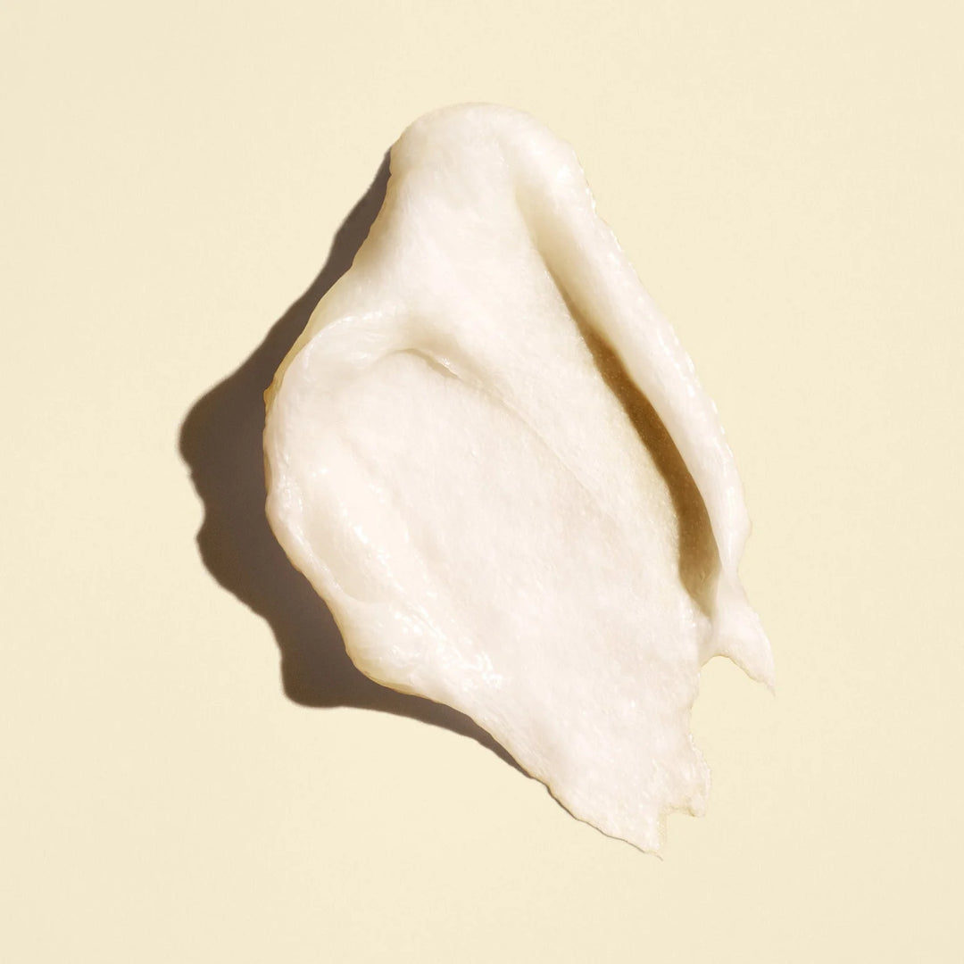 Texture crémeuse et épaisse de couleur blanc ivoire du masque capillaire ORIBE Gold Lust Transformative Masque, étalée sur un fond beige clair.
