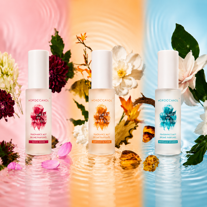 Collection de brumes parfumées Moroccanoil Brumes du Maroc pour cheveux et corps, bouteilles givrés rose, orange et turquoise sur fond floral aquatique lumineux.
