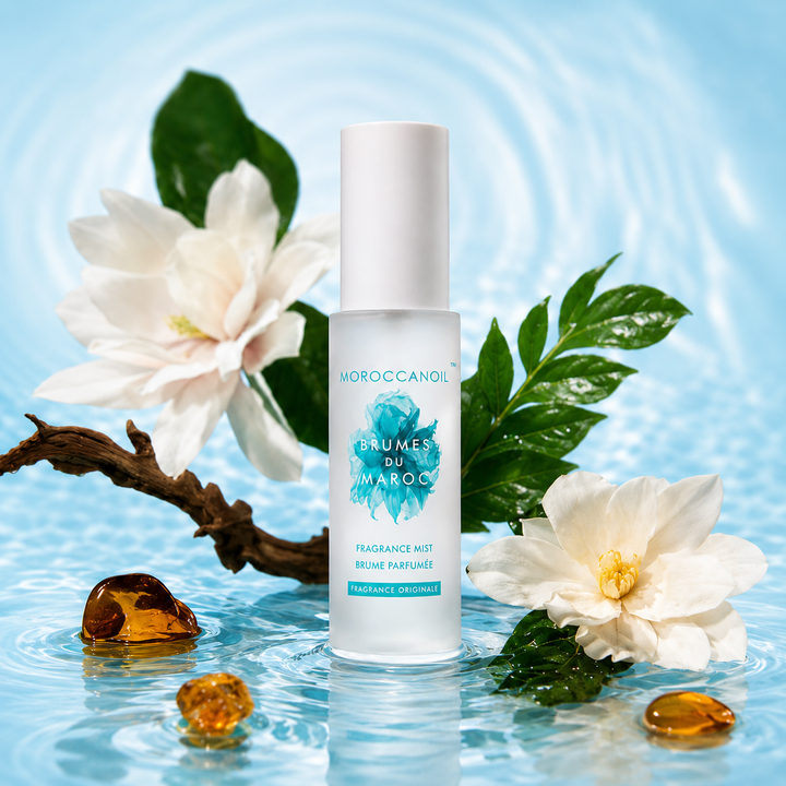 Brume parfumée Moroccanoil Fragrance Originale 100 ml dans bouteille givrée turquoise avec fleurs blanches, feuilles vertes et fond bleu aquatique élégant.