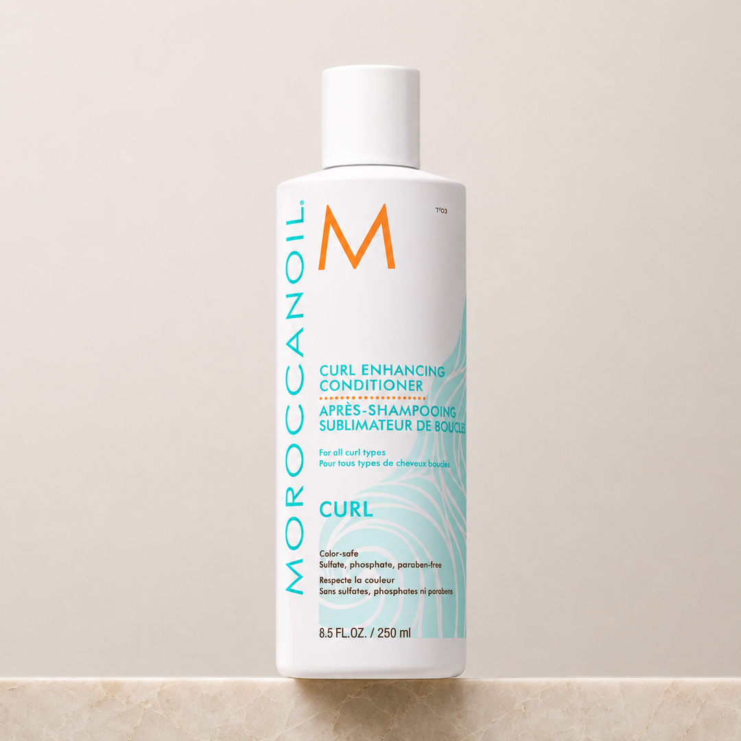 Après-shampoing Sublimateur de Boucles Moroccanoil 250 ml en bouteille blanche avec bouchon blanc, étiquette turquoise, présenté sur un comptoir de pierre beige avec fond neutre.