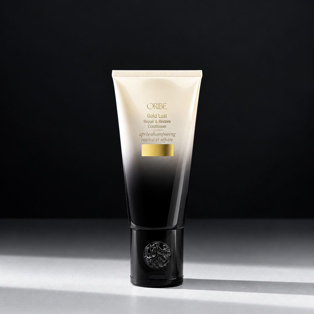 Tube d'après-shampoing ORIBE Gold Lust Repair & Restore, dégradé ivoire et noir, détails dorés et bouchon noir orné du logo, sur fond sombre.