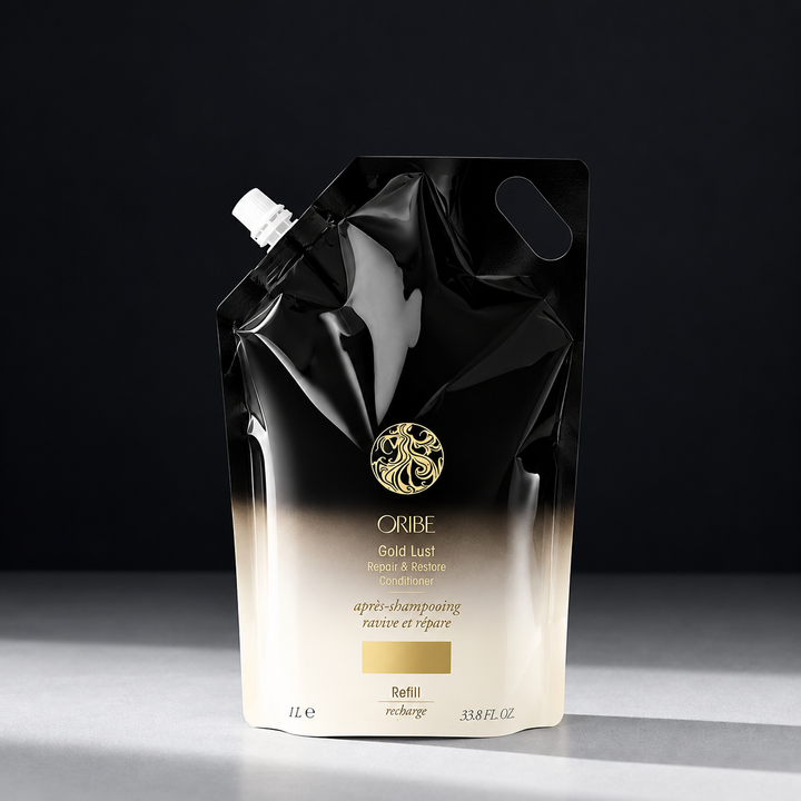Recharge ORIBE Gold Lust Repair & Restore Conditioner 1 L, sachet souple noir et ivoire avec bouchon blanc, logo doré, photographié sur fond sombre.