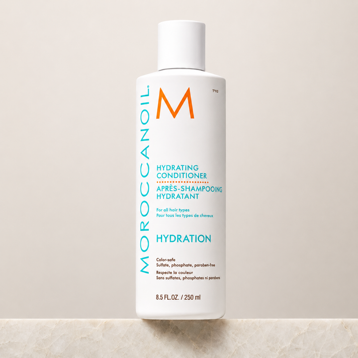Après-shampoing hydratant Moroccanoil Hydration 250 ml en bouteille blanche avec bouchon blanc, posé sur un fond beige minimaliste, photo produit professionnelle.